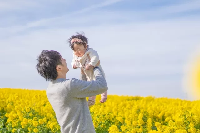 菜の花畑で赤ちゃんを抱っこするパパ